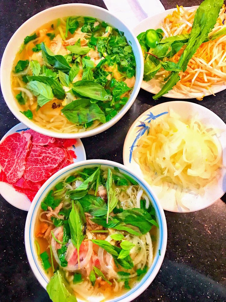 Two bowls of pho with herbs, rare beef and lime